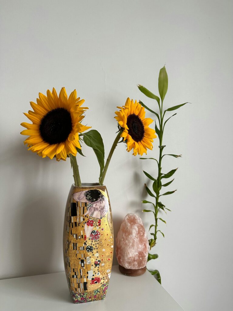 Sunflowers in a Klimt-inspired vase with a salt lamp and bamboo plant in the background.