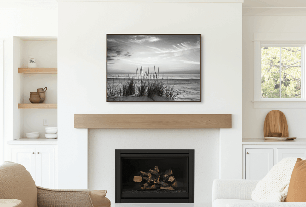 A modern living room with a black and white landscape painting above a wooden mantelpiece, with white walls and wooden accents