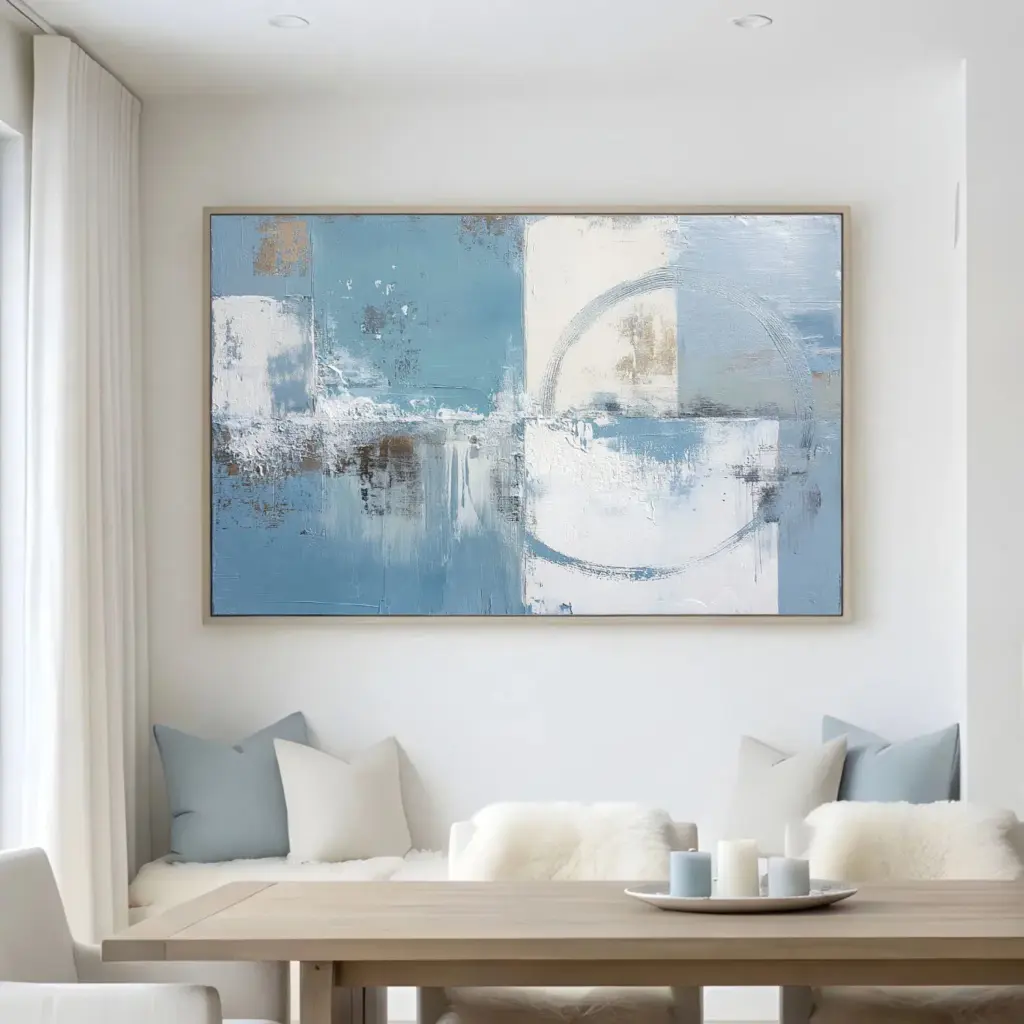 Abstract blue and white painting above living room table – A neutral-toned living area with a rectangular abstract painting in light blues and whites mounted above a small dining or console table.
